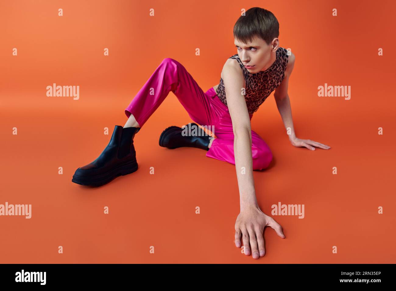 queer person in leopard print top and pink pants sitting on orange