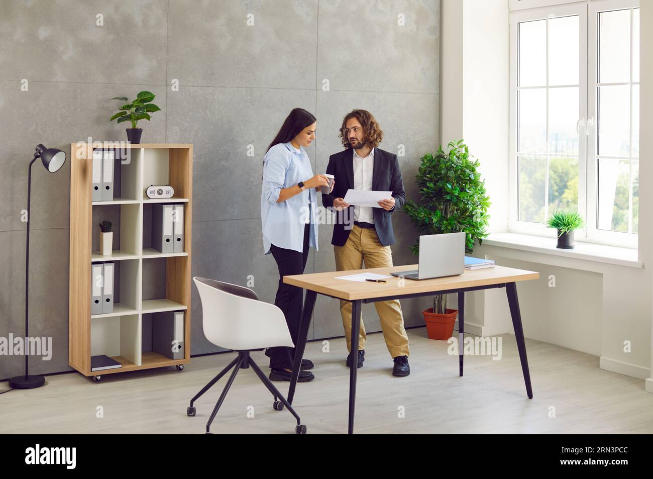 Two business people man and woman standing in office near the workplace and talking. Stock Photo