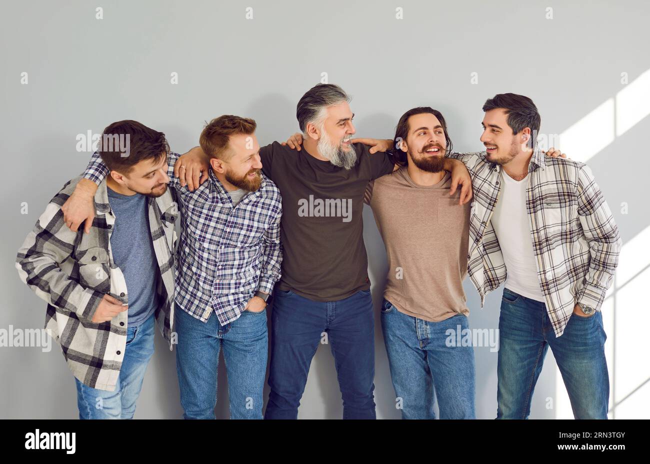 Male bearded friends looking cheerful to each other and smiling on grey ...