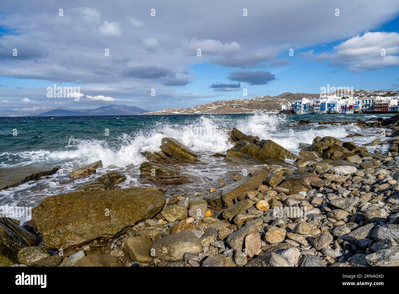 Waves breaking between the rocks on the beach, white Cycladic houses in ...
