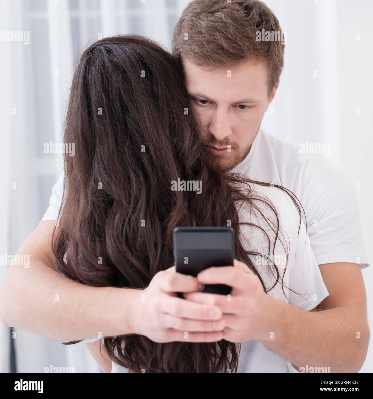 Man hugging his girlfriend while checking his phone Stock Photo