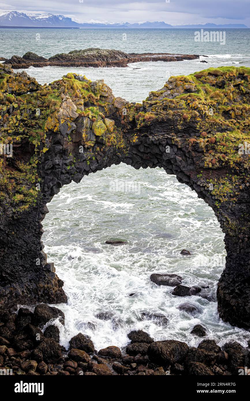 Lichen and moss covered stone bridge at Arnarstapi, Snaefellsness Peninsula, Iceland. The sea arch is known as Gatklettur, or the Hellnar Arch. Stock Photo