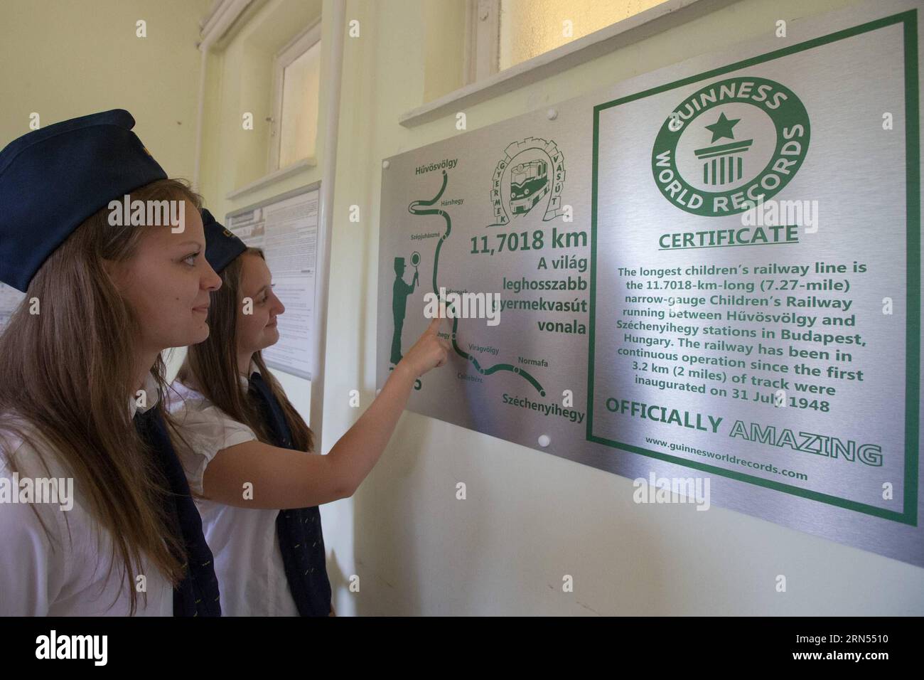 (150613) -- BUDAPEST, June 13, 2015 -- Girls watch the Guinness World Record plaque at Huvosvolgy station of the Children s Railway in Budapest, Hungary, June 13, 2015. The 11.7018 km narrow-gauge railway runs between Huvosvolgy and Szechenyihegy stations in Budapest. It has been in continuous operation since the first 3.2 km of track were inaugurated on July 31, 1948. The engines are driven by adult engineers, and children aged 10 to 14 on duty are continuously supervised by adult railway employees. Apart from that, children do their jobs on their own. The Children s Railway has received the Stock Photo