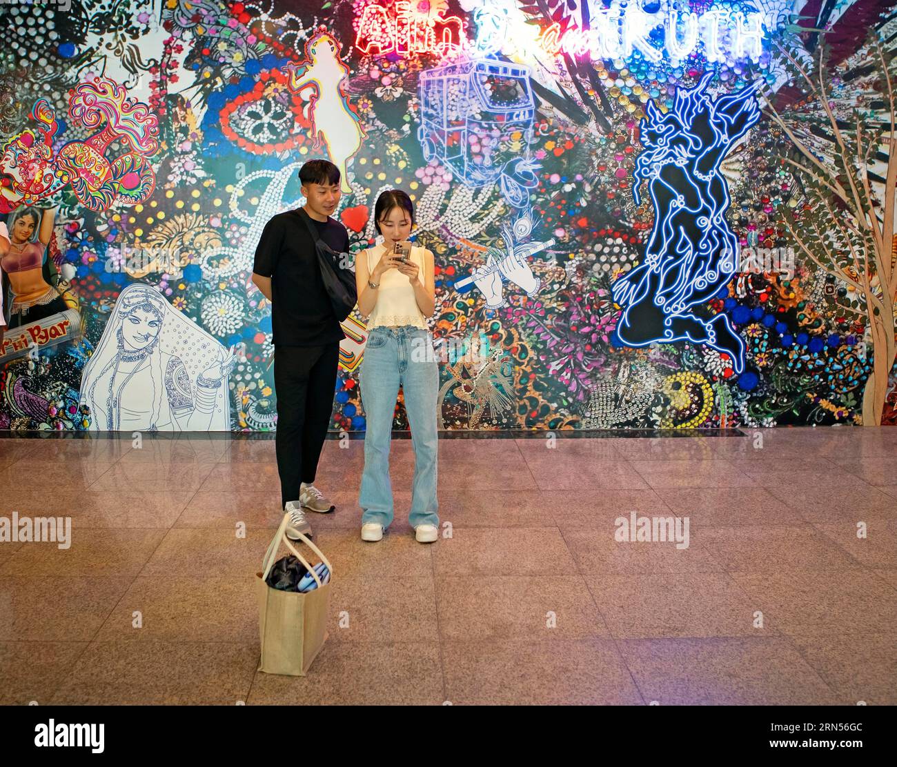 Korean couple looking at a smartphone, Korean artwork behind, Biennale 2023, Gwangju, Jeollanam-do Province, South Korea Stock Photo