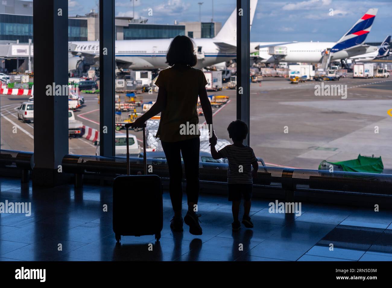 Silhouette of mother and son with luggage standing near the window in the airport, vacation concept Stock Photo