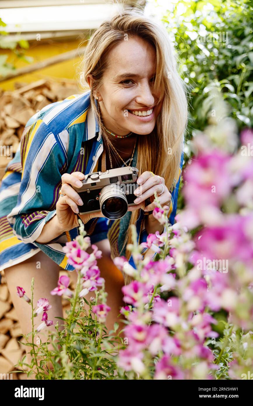 Germany, young woman photographing blooming flowers in the garden, portrait, camera, photography, smile, young woman, blonde, caucasian, desire Stock Photo