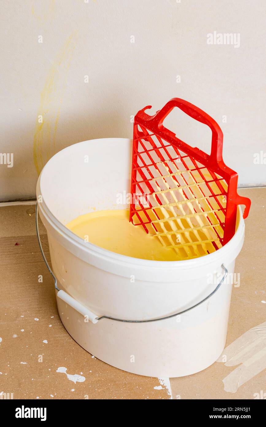 Scraper grid in bucket with yellow wall paint, painting work Stock
