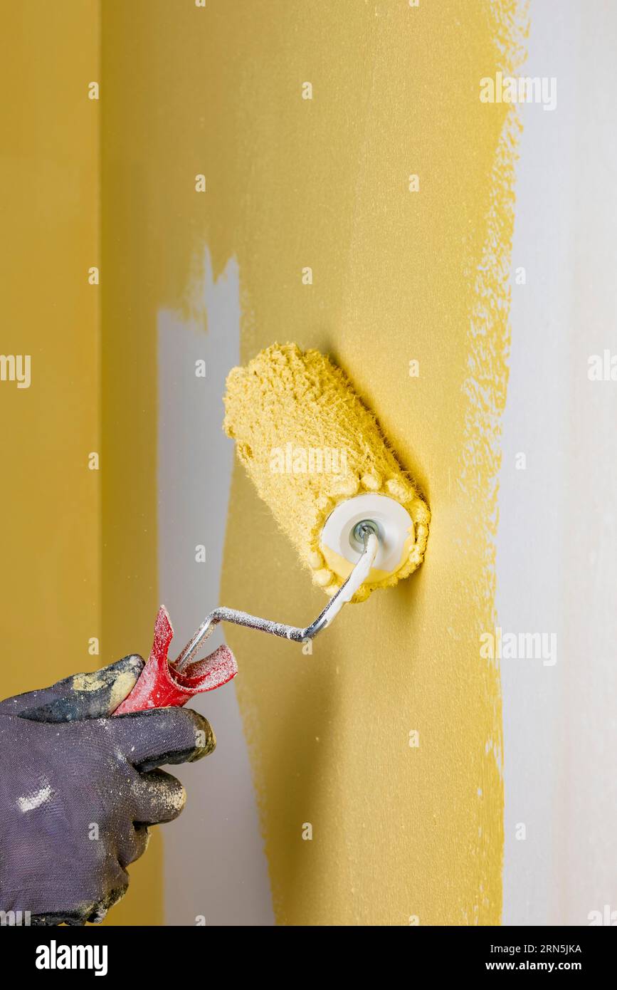 Wall is painted with yellow paint, hand with paint roller Stock Photo
