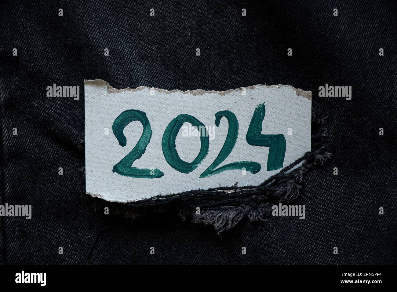 2024 is written in green paints on a paper card that lies on black denim, happy new year 2024, banner and background Stock Photo