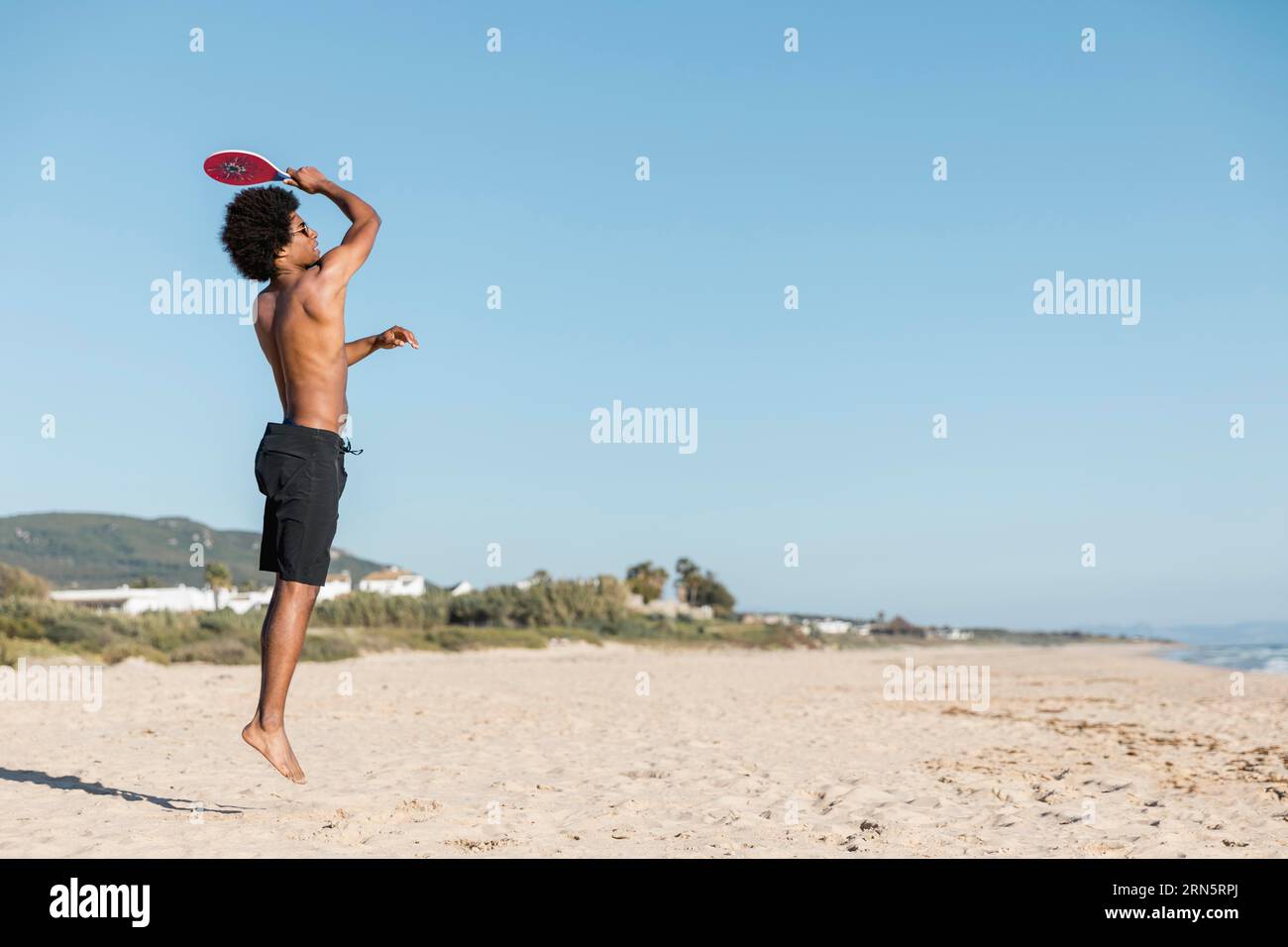 Man jumping with tennis racket beach Stock Photo