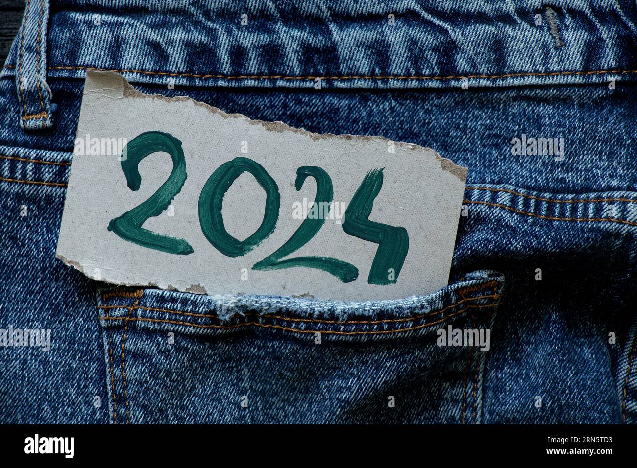 2024 is written in green paints on a paper card that lies in a jeans pocket, Happy New Year 2024, banner and background Stock Photo