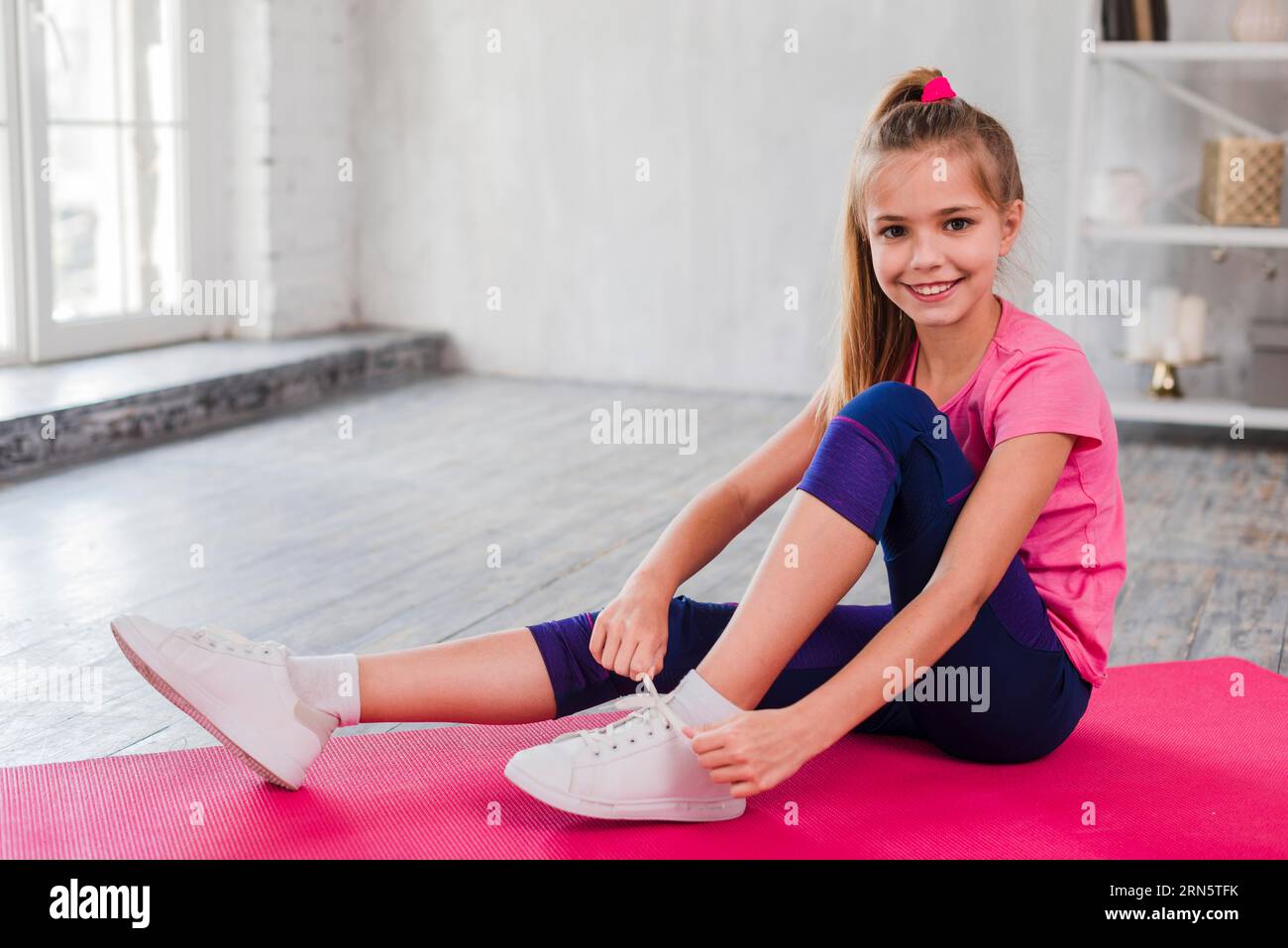 Portrait smiling girl sitting exercise mat tying her shoelace Stock Photo