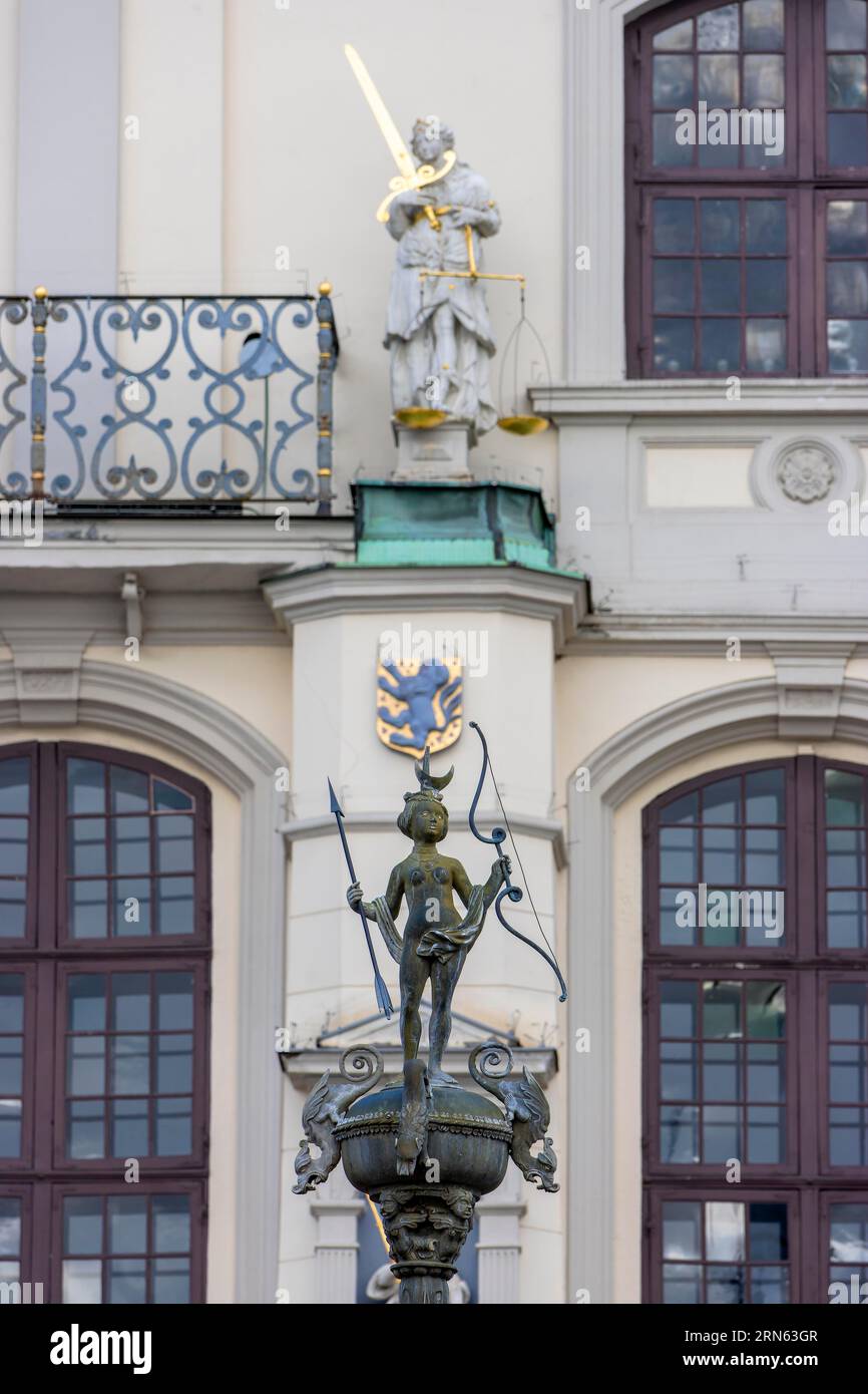 Detail of the bronze statue of the goddess Artemis with bow and arrow on the Lunabrunnen and in the background a sculpture on the facade of the town Stock Photo