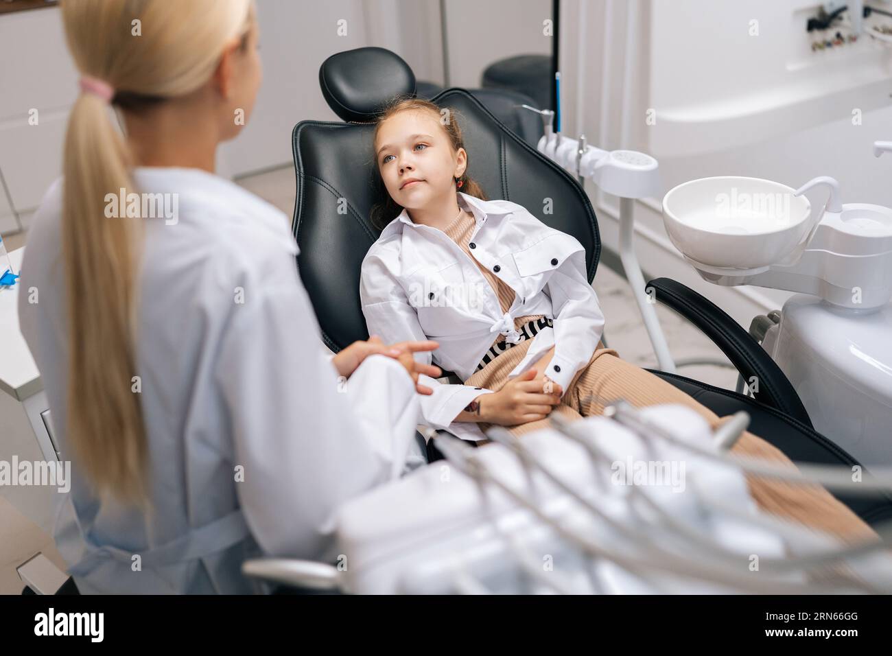 Back view of cute little girl sitting on dental chair and complaining
