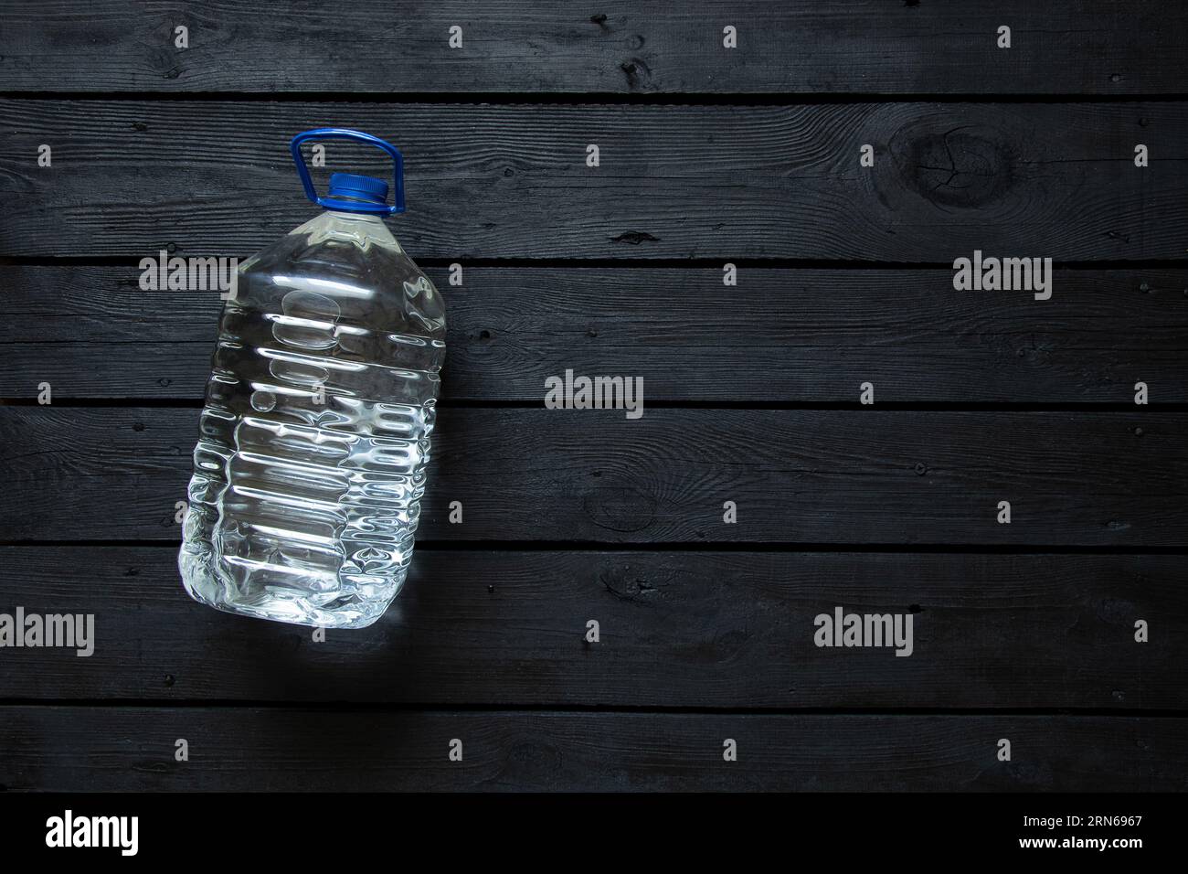 A five-liter plastic water bottle lies on a black wooden board, bottled water Stock Photo