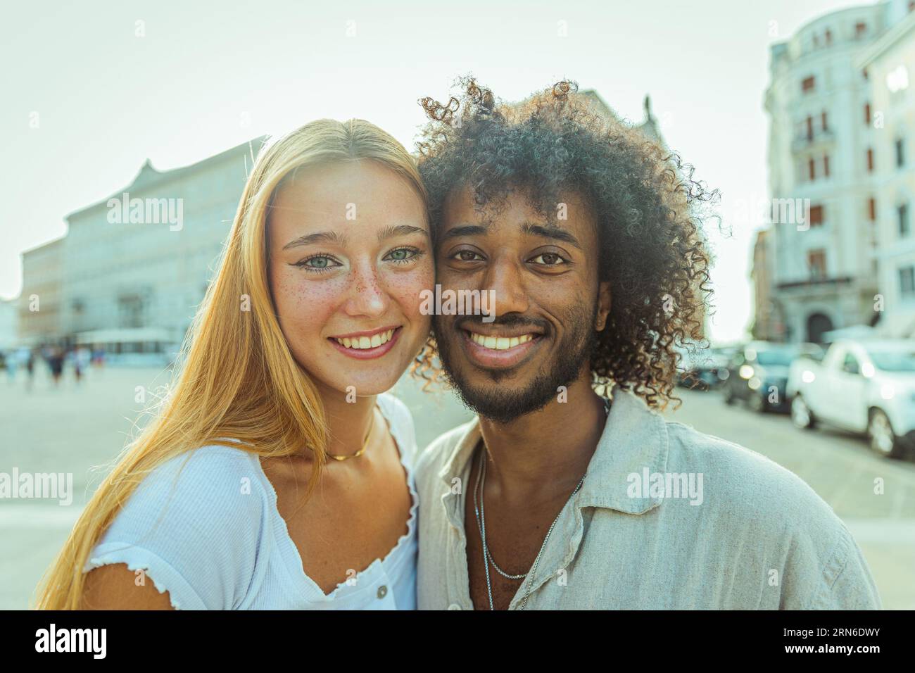 Portrait of two young adults of different ethnic backgrounds smiling in the summer in the city Stock Photo
