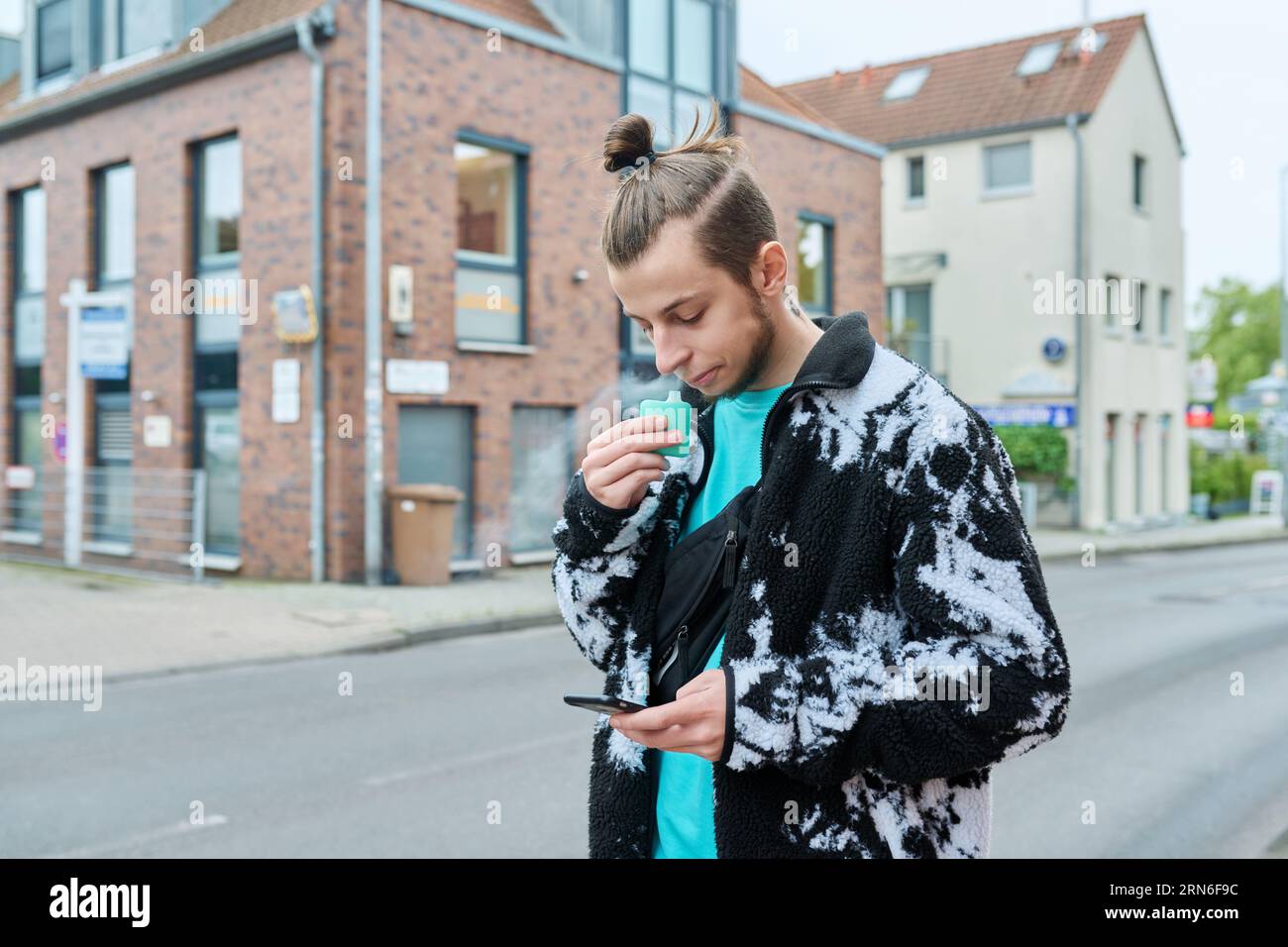 Young hipster male using smartphone, smoking disposable electronic cigarette Stock Photo