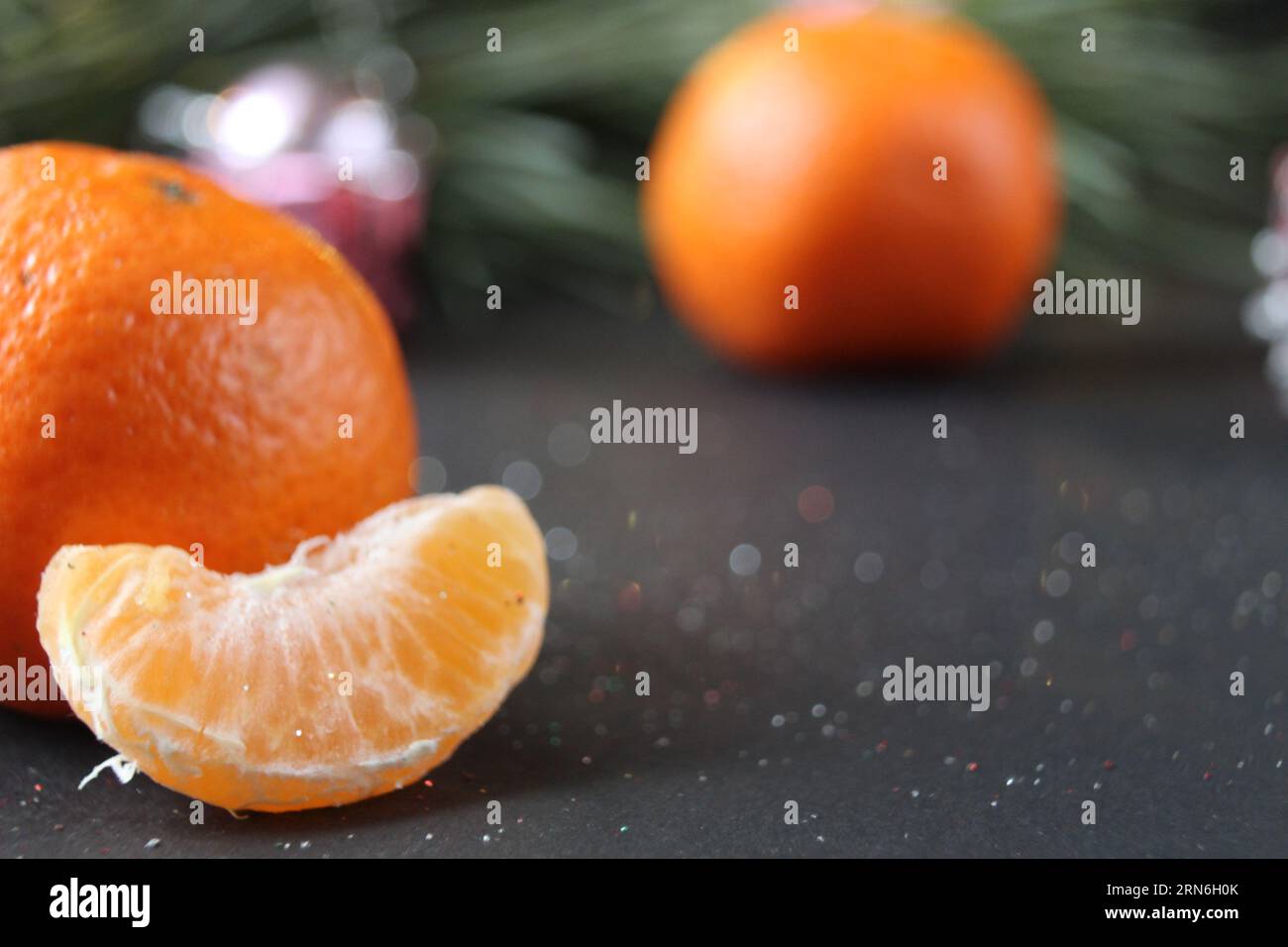 mandarin whole in the peel and a slice of fruit lie side by side on a black background next to a branch of spruce and a silver cone. New Year and Chri Stock Photo