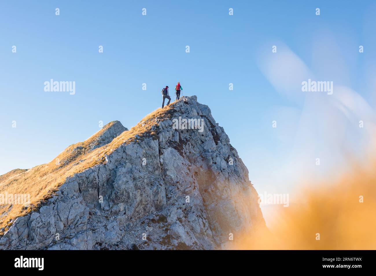 Spectacular view of two hikers walking along the mountain ridge route with the sun on the clear blue sky, aerial shot. Inspiration, nature, and Stock Photo