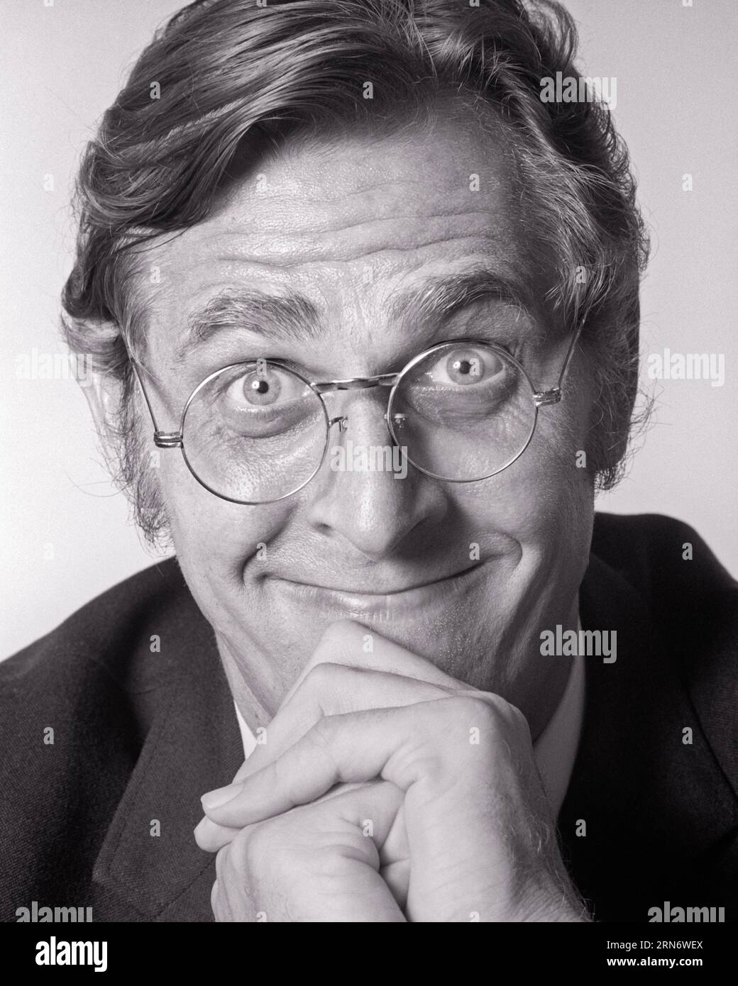 1970s PORTRAIT MAN RESTING HIS CHIN ON CLASPED HANDS SMILING WEARING ROUND METAL FRAME EYEGLASSES FUNNY FACIAL EXPRESSION - p7960 HAR001 HARS SATISFACTION STUDIO SHOT COPY SPACE ASKING PERSONS MALES CHIN CONFIDENCE EYEGLASSES EXPRESSIONS B&W RESTING WIDE EYE CONTACT BIZARRE BUG-EYED HUMOROUS STARING HAPPINESS WEIRD HEAD AND SHOULDERS CHEERFUL HIS GROTESQUE EXCITEMENT ZANY COMICAL UNCONVENTIONAL ANTICIPATION SMILES CLASPED COMEDY JOYFUL WACKY IDIOSYNCRATIC WIDE-EYED AMUSING EAGER ECCENTRIC GRIN MID-ADULT MID-ADULT MAN QUESTIONING STARTLED WIRE FRAME BLACK AND WHITE CAUCASIAN ETHNICITY ERRATIC Stock Photo
