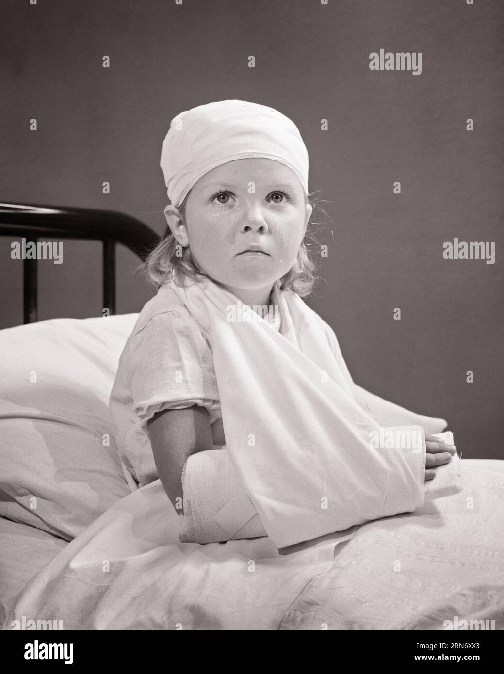1940s SAD INJURED LITTLE GIRL IN HOSPITAL BED WITH BROKEN BANDAGED ARM