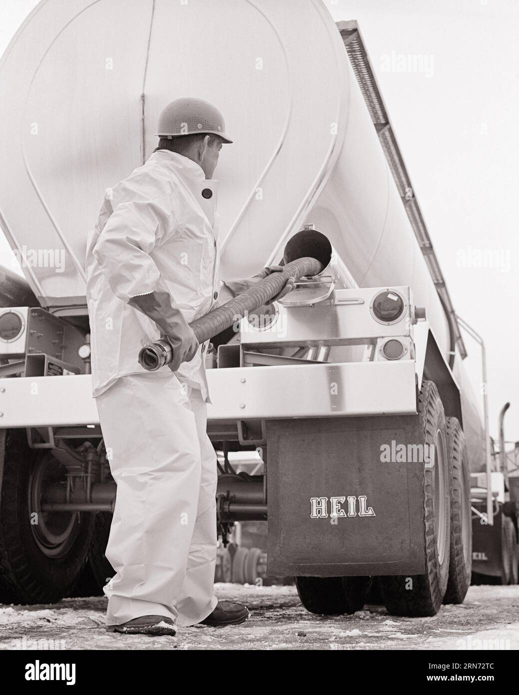 1970s WORKER WEARING PROTECTIVE GEAR HANDLING HOSE STORED IN A BULK LIQUID CHEMICAL TANK TRUCK USED TO LOAD OR OFF LOAD CARGO - m9616 HAR001 HARS LABORING OLD FASHIONED Stock Photo