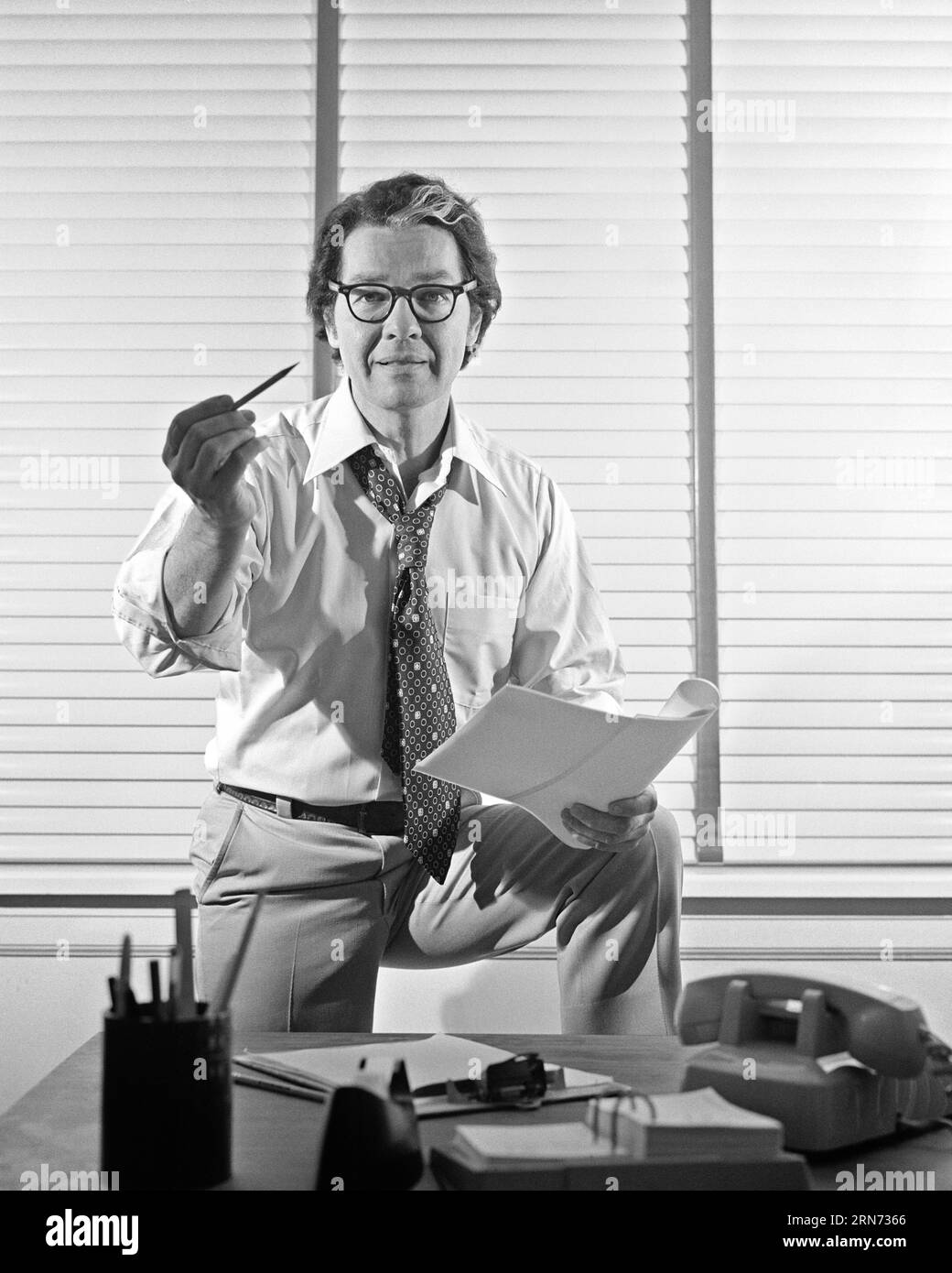 1970s BUSINESSMAN AT DESK WEARING EYEGLASSES NECKTIE LOOSENED SHIRT SLEEVES ROLLED UP HOLDS PENCIL IN ONE HAND PAPERS IN OTHER  - o4155 HAR001 HARS ROLLED STUDIO SHOT MANAGER COPY SPACE HALF-LENGTH PERSONS THOUGHTFUL MALES CONFIDENCE EXECUTIVES EYEGLASSES GESTURING B&W EYE CONTACT STRATEGY EXCITEMENT LEADERSHIP DIRECTION UP GESTURES NECKTIE OCCUPATIONS BOSSES CONCEPTUAL SLEEVES SINCERE LOOSENED SOLEMN FOCUSED GRAY STREAK HOLDS INTENSE MANAGERS MID-ADULT MID-ADULT MAN SOLUTIONS BLACK AND WHITE CAREFUL CAUCASIAN ETHNICITY EARNEST HAR001 INTENT OLD FASHIONED Stock Photo