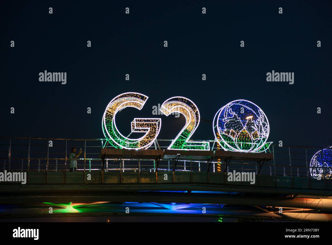 New Delhi, India. 31st Aug, 2023. A man takes photos with illuminated G20 logo installed on pedestrian bridge outside the main venue near Pragati Maidan. The G20 (Global economic cooperation forum of 19 individual countries) Summit, which is scheduled to be held in New Delhi on September 9th and 10th 2023, will be attended by several world leaders, who are a part of the grouping. This year will be the 18th G20 Summit and India's first in terms of presidency. Credit: SOPA Images Limited/Alamy Live News Stock Photo