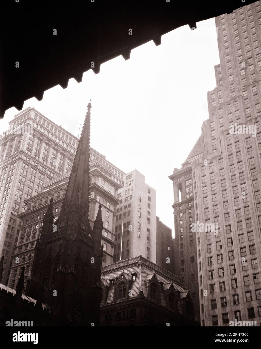 1920s SPIRE OF TRINITY CHURCH IN CENTER OF BUILDINGS AT WALL STREET AND BROADWAY NEW YORK CITY NY USA - q2437 CPC001 HARS CITIES EDIFICE NEW YORK CITY FAITHFUL ARCHITECTURAL DETAIL BROADWAY FAITH BELIEF BLACK AND WHITE FINANCIAL DISTRICT OLD FASHIONED SPIRE TRINITY Stock Photo