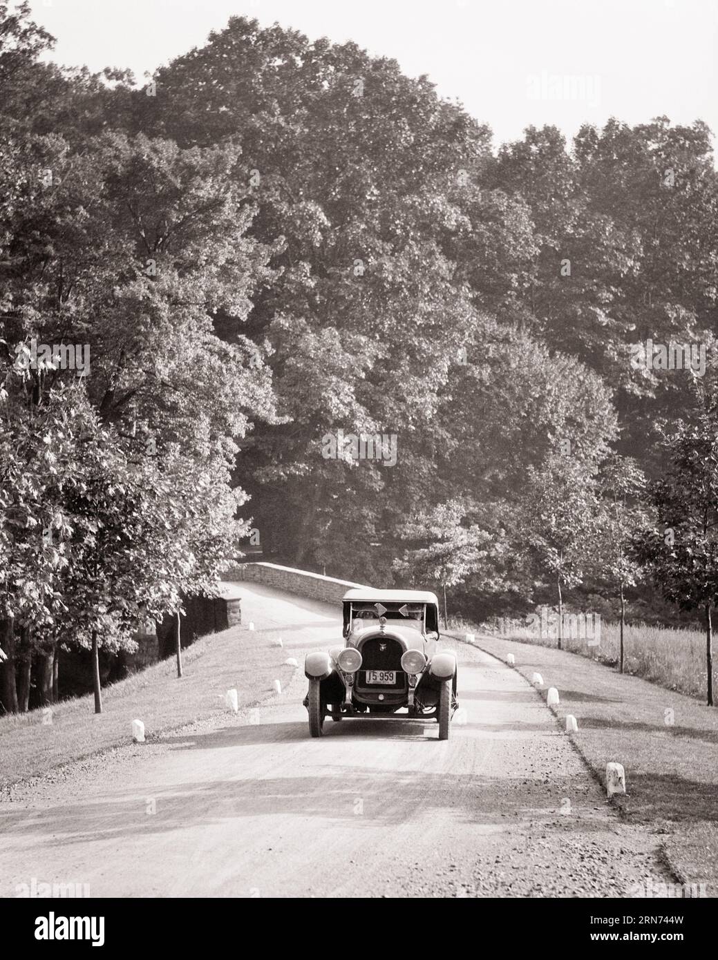 1920s ANTIQUE CONVERTIBLE TOURING CAR AUTOMOBILE ALONE ON NARROW COUNTRY LANE DRIVING TOWARDS THE CAMERA - m85 HAR001 HARS SUNDAY DRIVE CONCEPTUAL AUTOMOBILES ESCAPE STYLISH VEHICLES RELAXATION SEASON BLACK AND WHITE HAR001 OLD FASHIONED TOURING Stock Photo