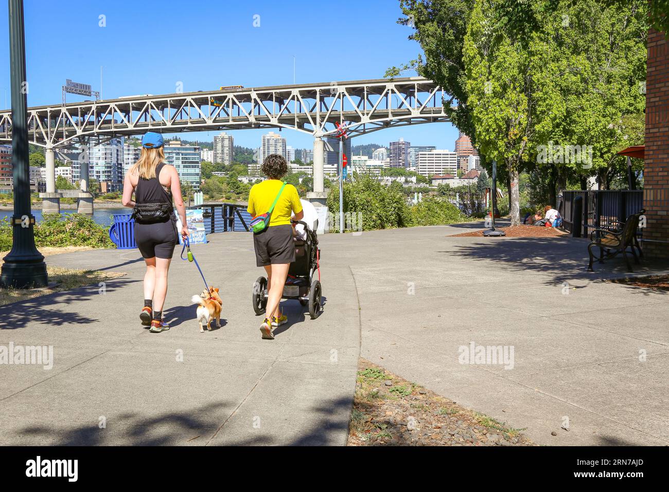 Two women walking with a baby stroller and a small dog on the Springwater Corridor Trail Near OMSI in downtown Portland Oregon waterfront Stock Photo