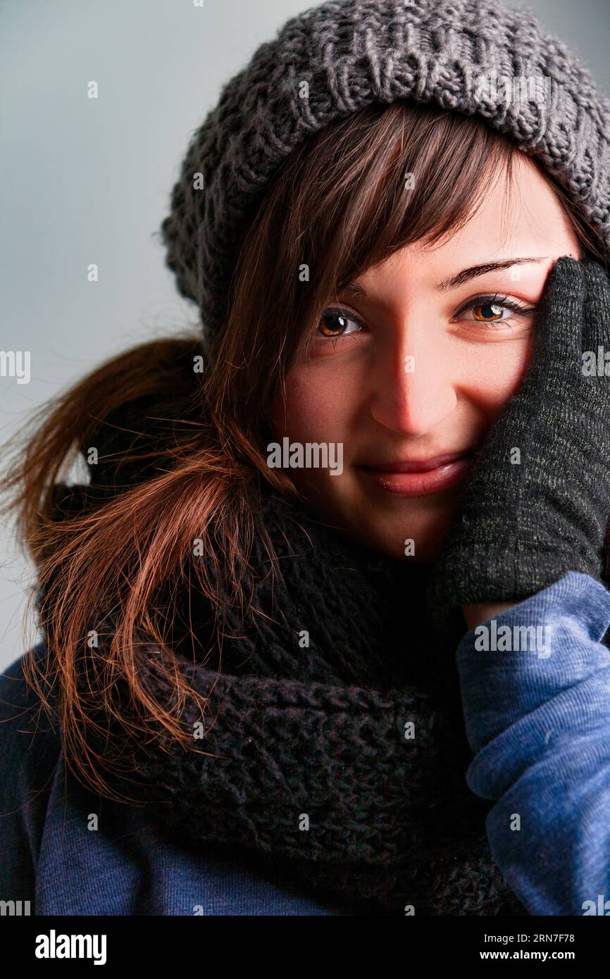 spirited young woman loves her winter fashion. Dressed in wool gloves, hat, scarf, and snug sweaters, she's warm despite the chill. Her long brown hai Stock Photo