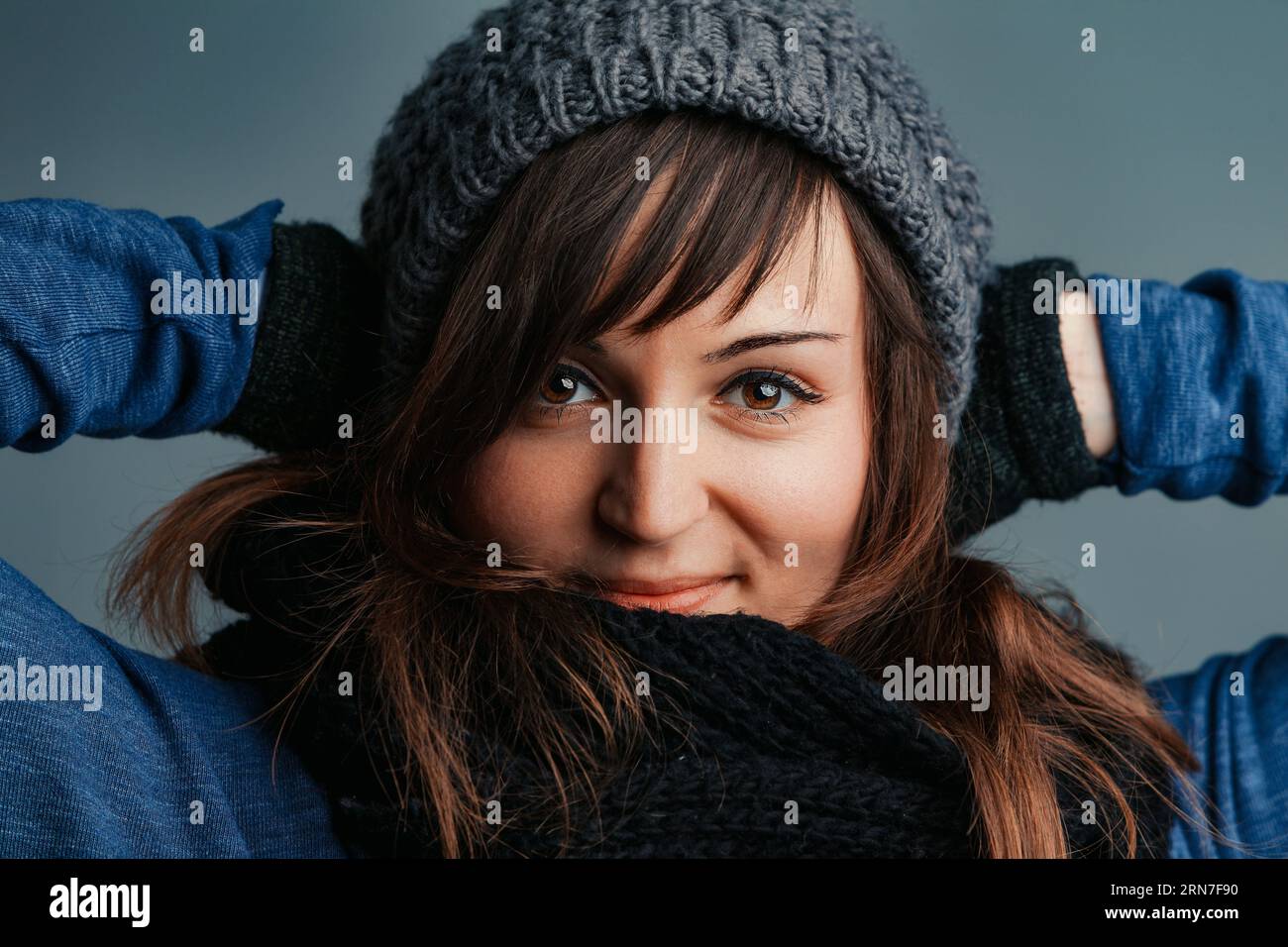 Regardless of the chill, a woman with long brown hair and vibrant eyes enjoys her winter outfits: wool gloves, scarf, and cozy jumpers Stock Photo