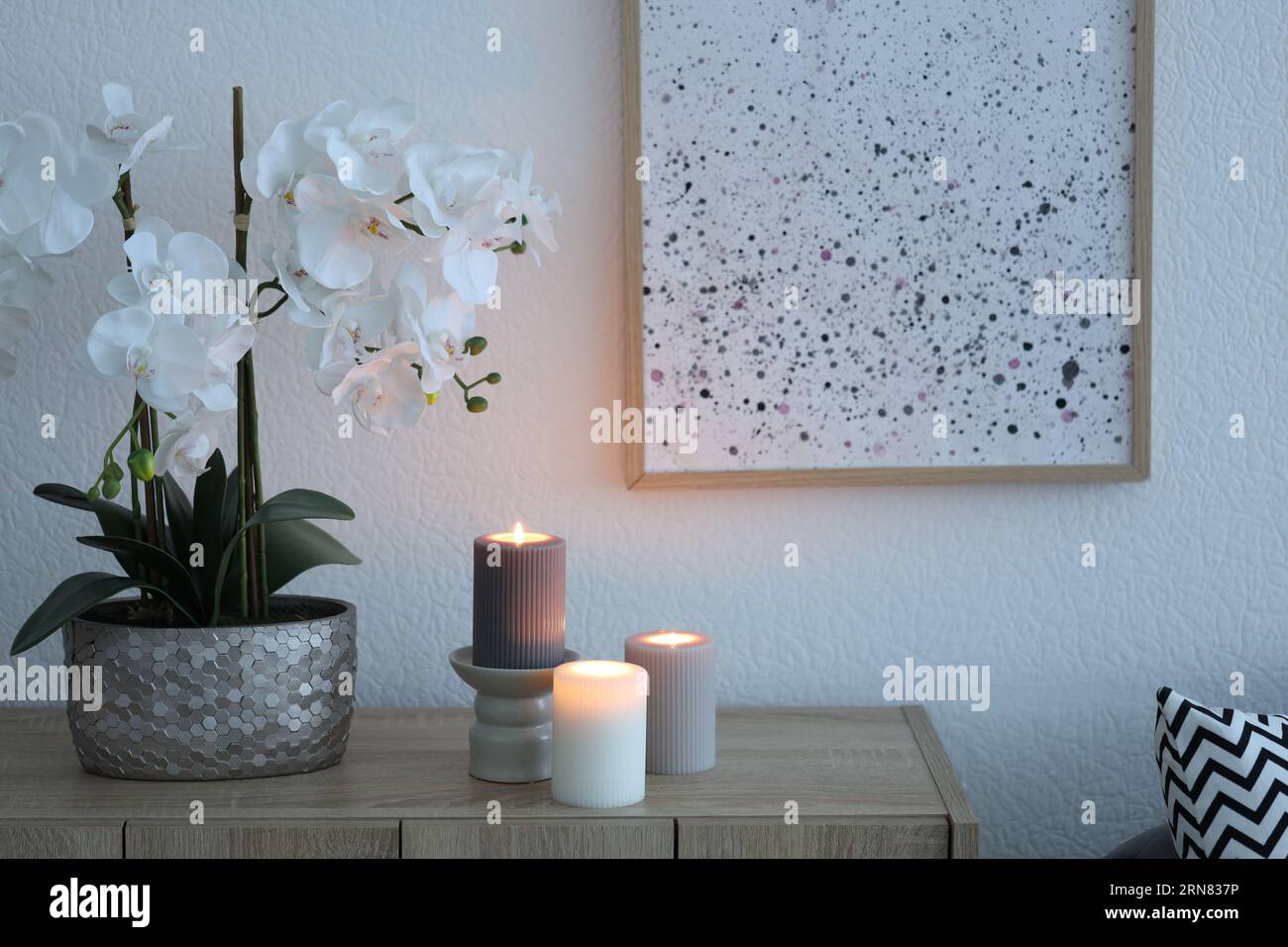 Beautiful orchid flowers and burning candles on wooden chest of drawers indoors Stock Photo