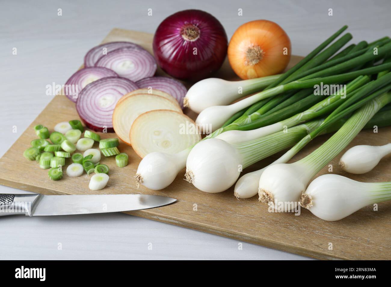 Board with different kinds of onions on white wooden table, closeup ...