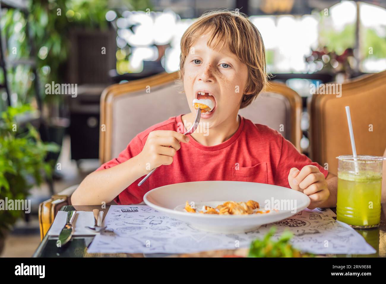 Portrait of small caucasian boy little child eating at restaurant in sunny day while sitting by the table alone - healthy eating growing up concept Stock Photo