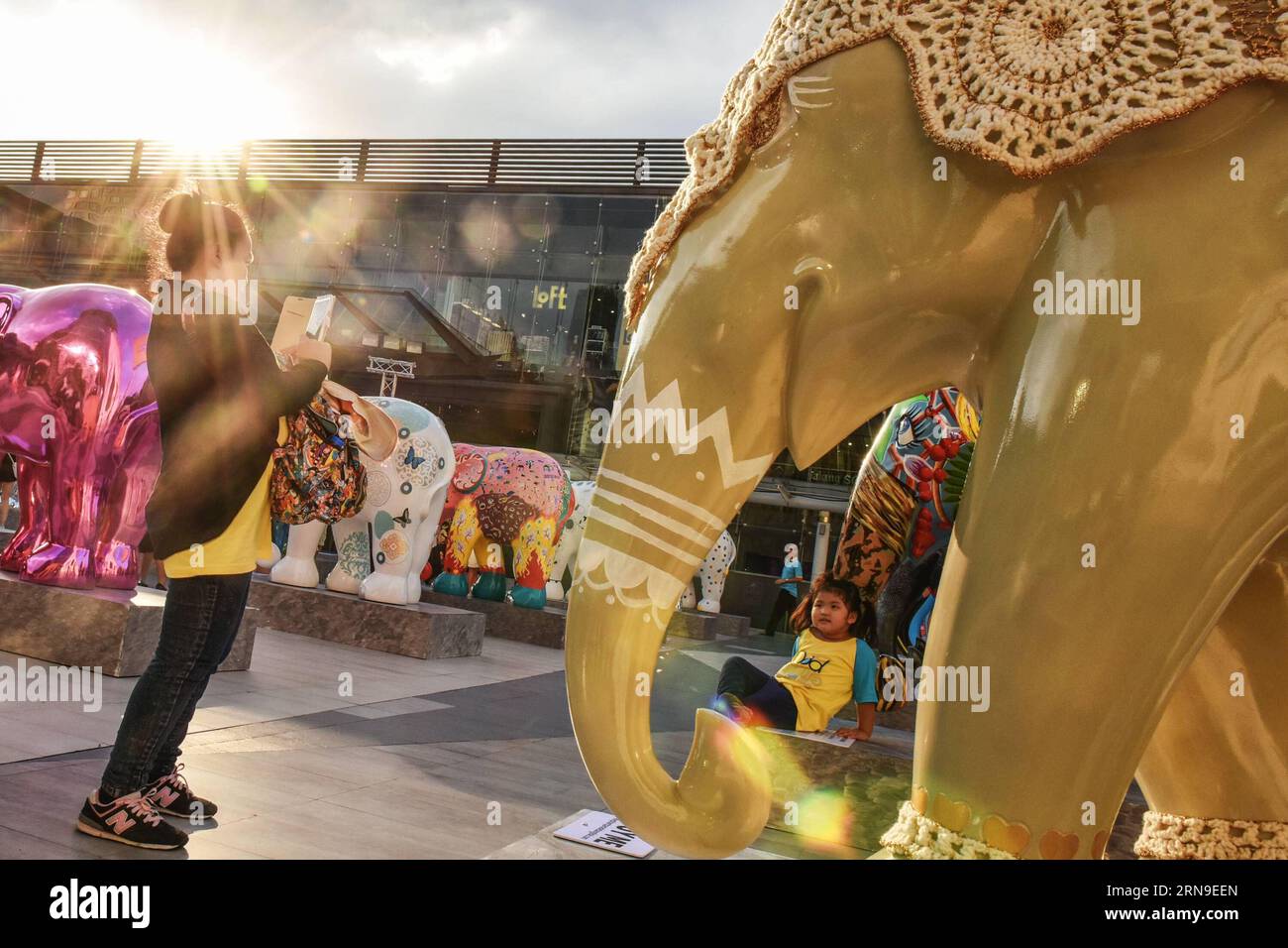 (151201) -- BANGKOK, Dec. 1, 2015 -- A woman takes photos for her child during the Elephant Parade Bangkok 2015 open-air exhibition in downtown Bangkok, capital of Thailand, on Dec. 1, 2015. Eighty-eight colored elephant statues created by various artists and celebrities were put on the show in Bangkok on Monday. Organized by Elephant Parade, a social enterprise, Elephant Parade Bangkok 2015 aims to raise awareness for the conservation and welfare of Asian elephants, an endangered species. All the elephant statues will be auctioned off and the proceeds will go to the Golden Triangle Asian Elep Stock Photo