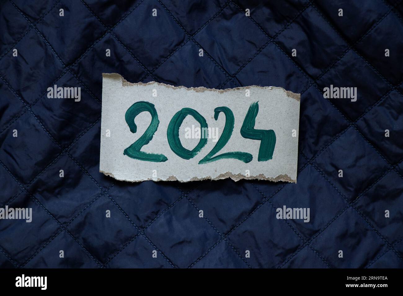 2024 is written in green ink on a paper card lying on a blue quilted background, Happy New Year 2024, banner and background Stock Photo