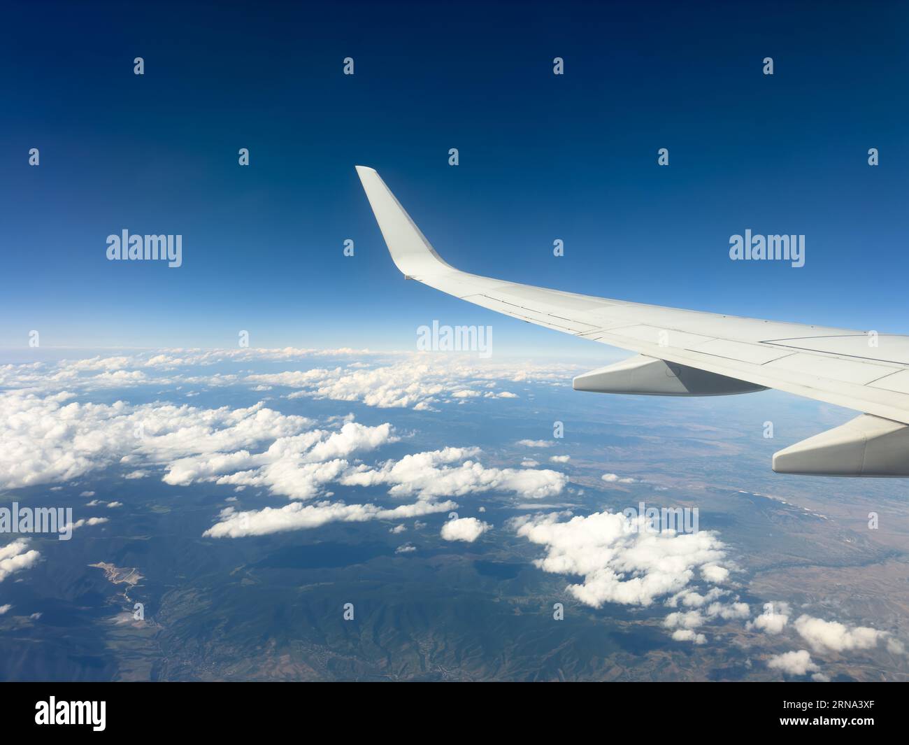 White wing from airplane window with mountain range below on sunny day ...