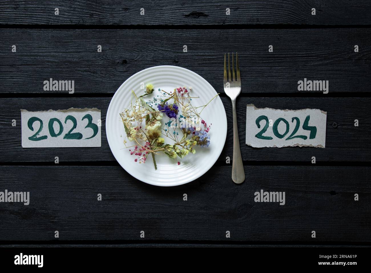 Postcards with the drawn text 2023 2024, and between them lies a plate of flowers and a fork, Happy New Year, festive table, holiday Stock Photo