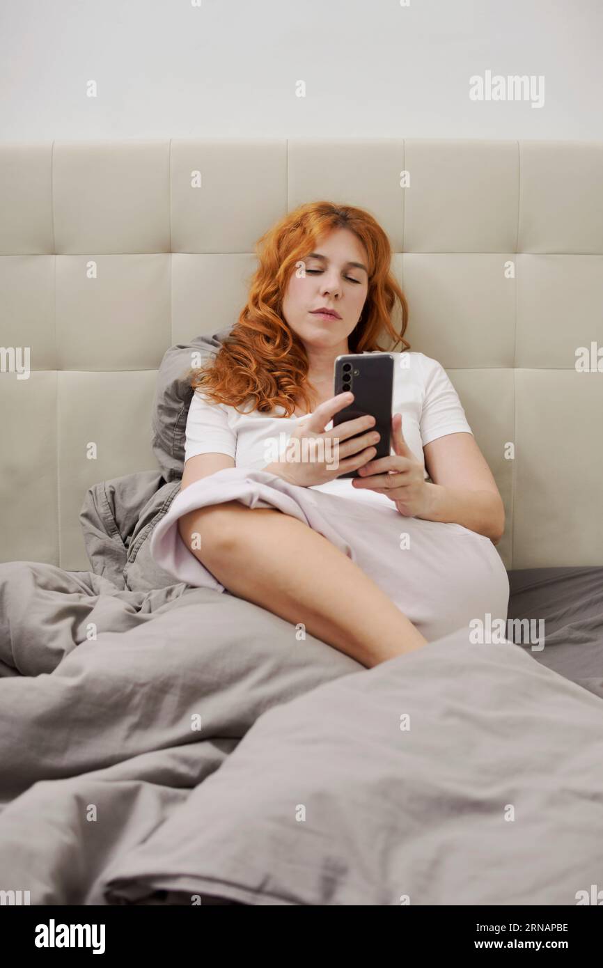 woman sitting in bed looking at her cell phone Stock Photo