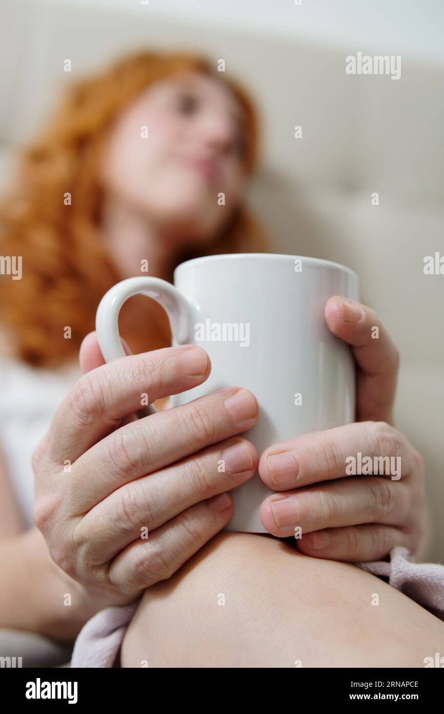 hands with cup in foreground with woman out of focus Stock Photo