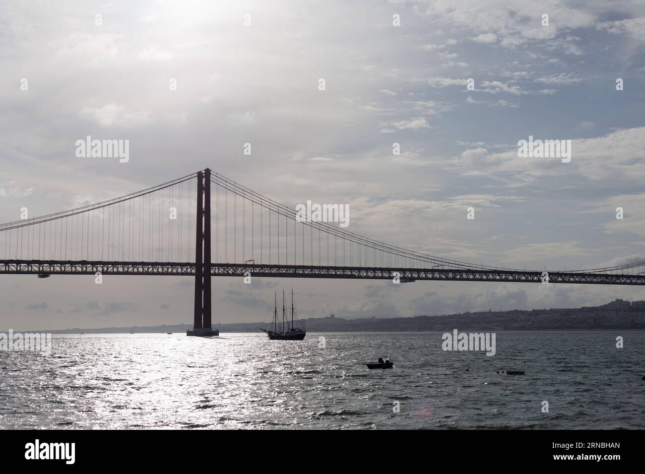 A scenic view of a boat sailing under a bridge on a cloudy day Stock Photo