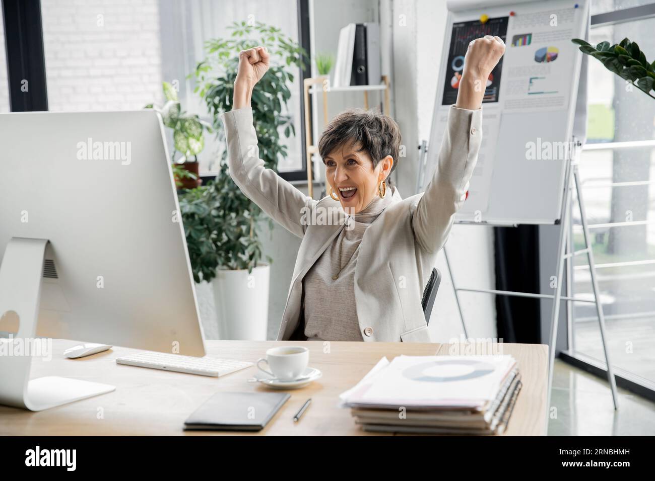excited entrepreneur showing win gesture near computer monitor in ...