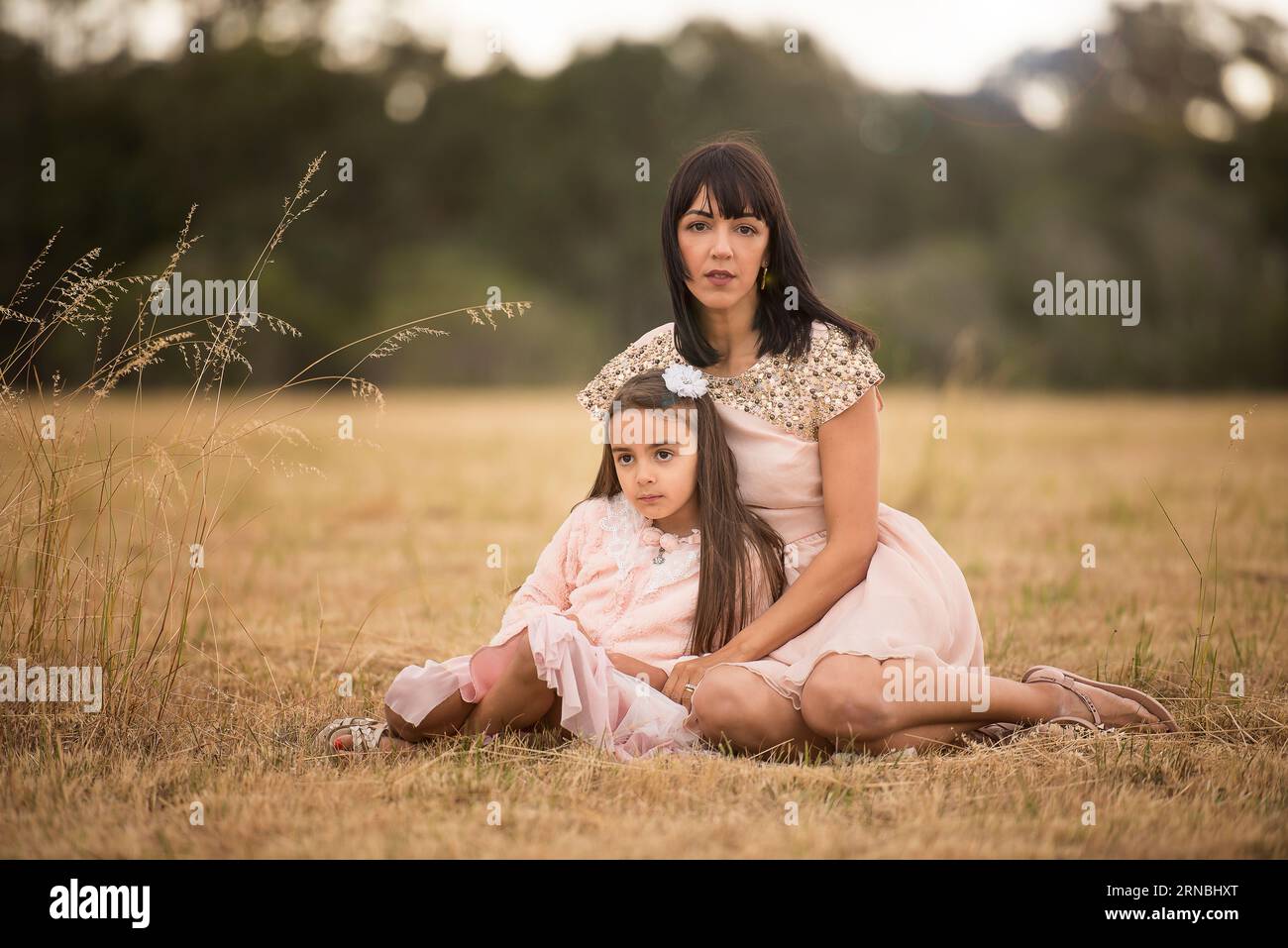Mother and daughter wearing pink sitting in open field afternoon Stock