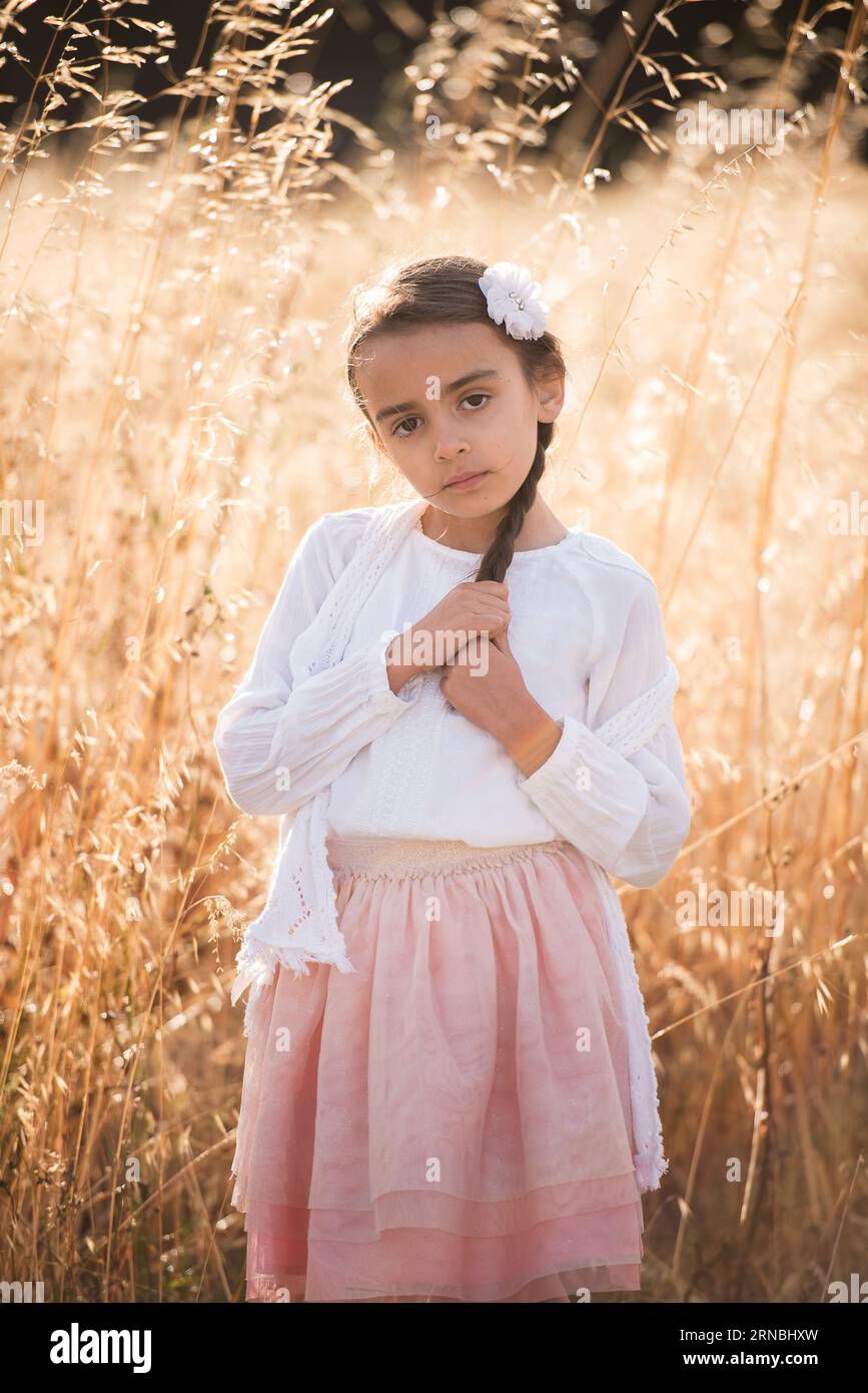 Little girl with braid in white top pink skirt in field of wheat Stock Photo