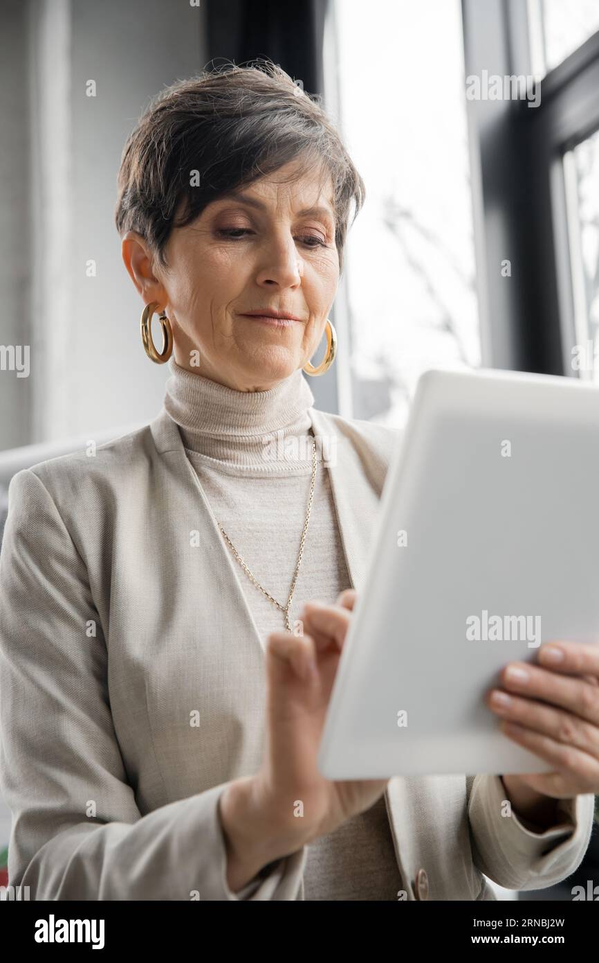 experienced middle aged entrepreneur using digital tablet in contemporary office, age in tech Stock Photo