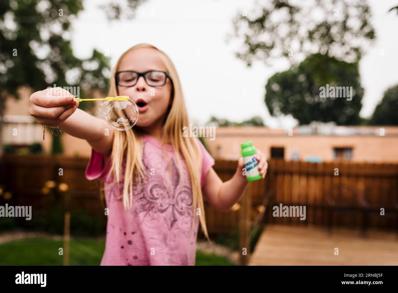 Little girl with glasses blows bubbles in North Dakota backyard summer Stock Photo