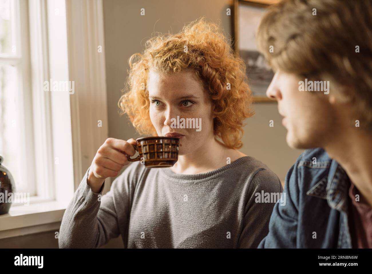 Young woman drinking coffee while sitting with crop friend Stock Photo