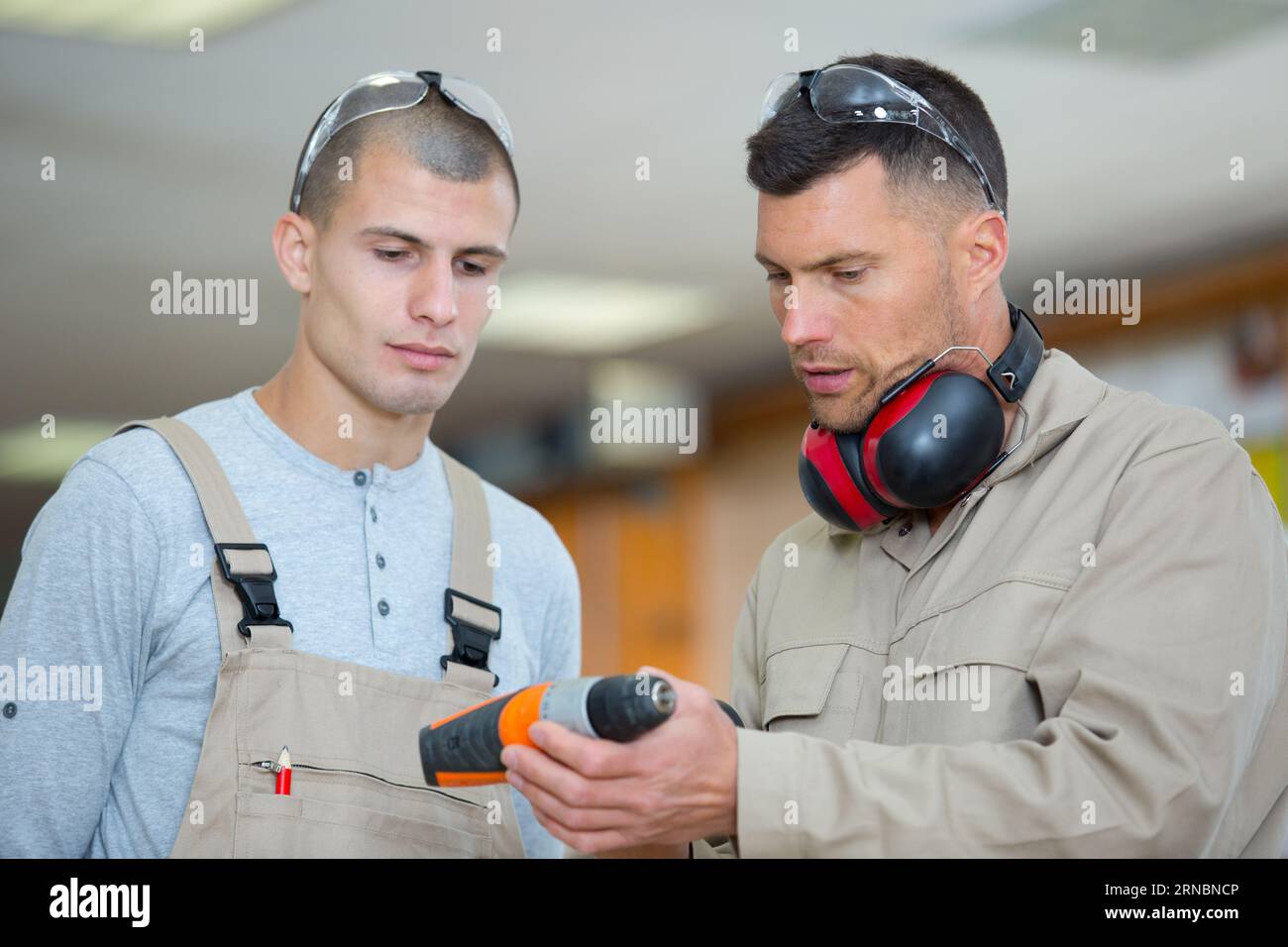engineer showing apprentice how to use drill in factory Stock Photo - Alamy